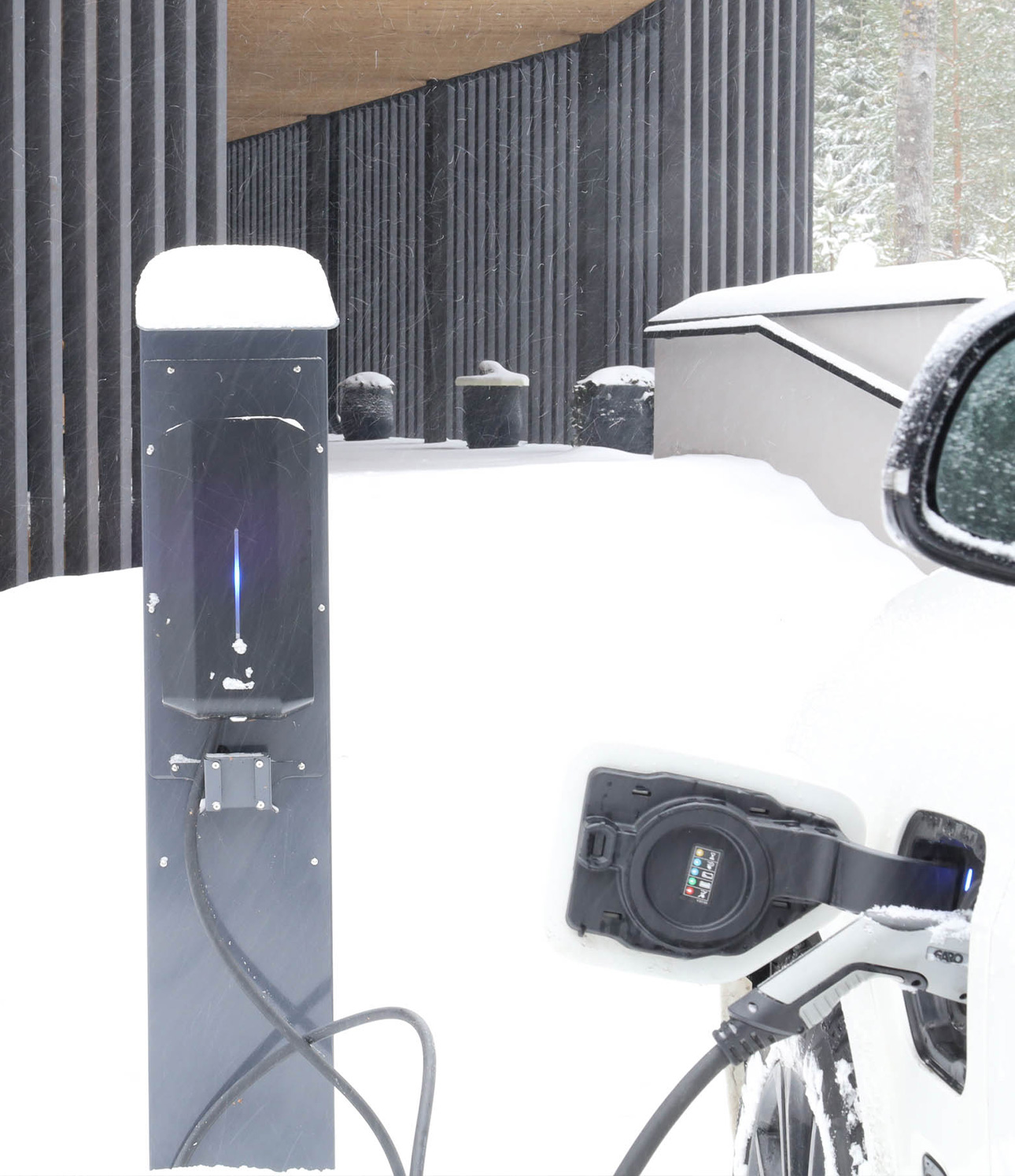 Sähköauton latausasema omakotitalon pihalla talvisessa maisemassa
